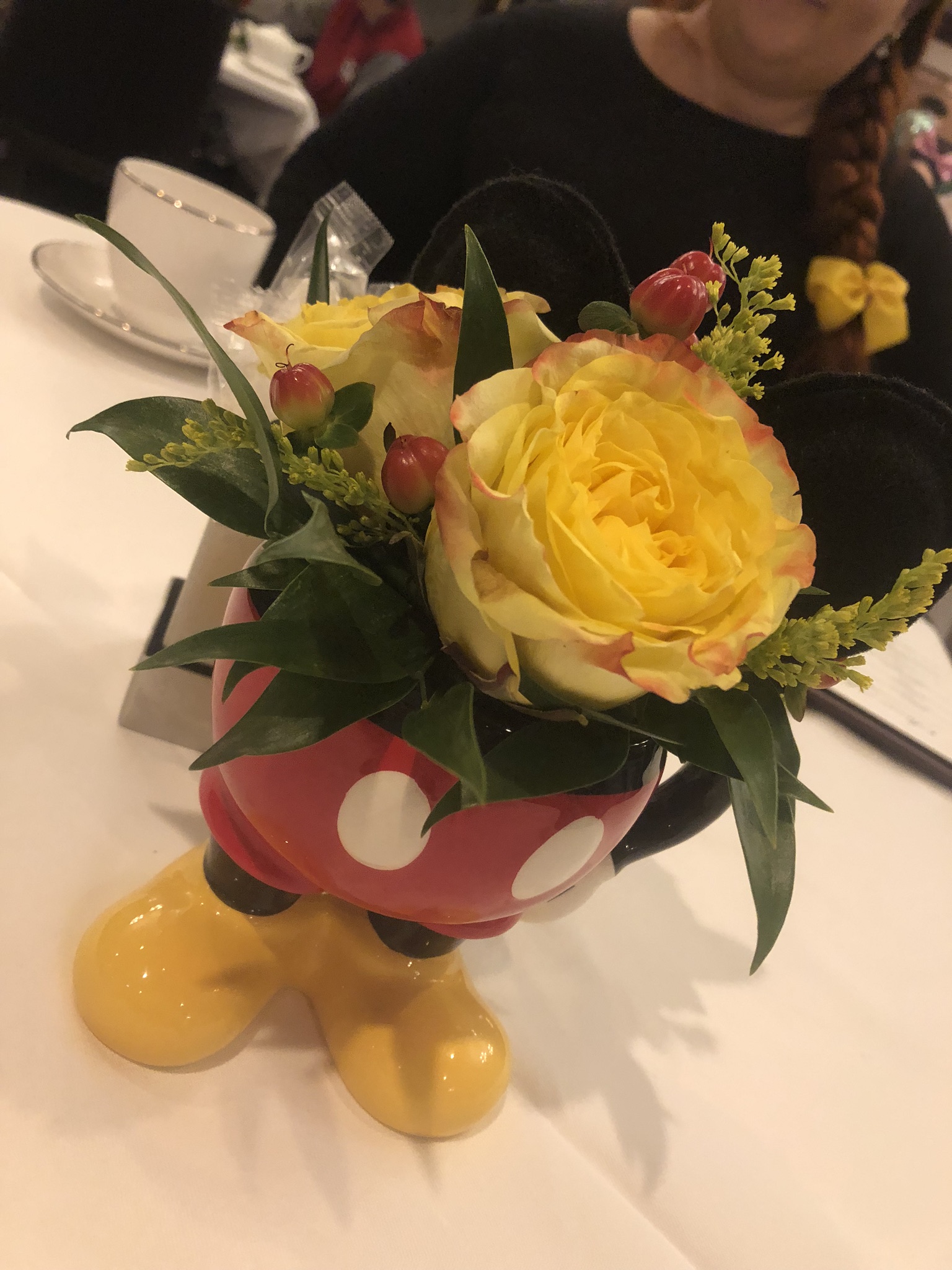 An image of a Mickey coffee mug, showcasing his iconic red shorts and yellow shoes, with yellow roses sticking out.