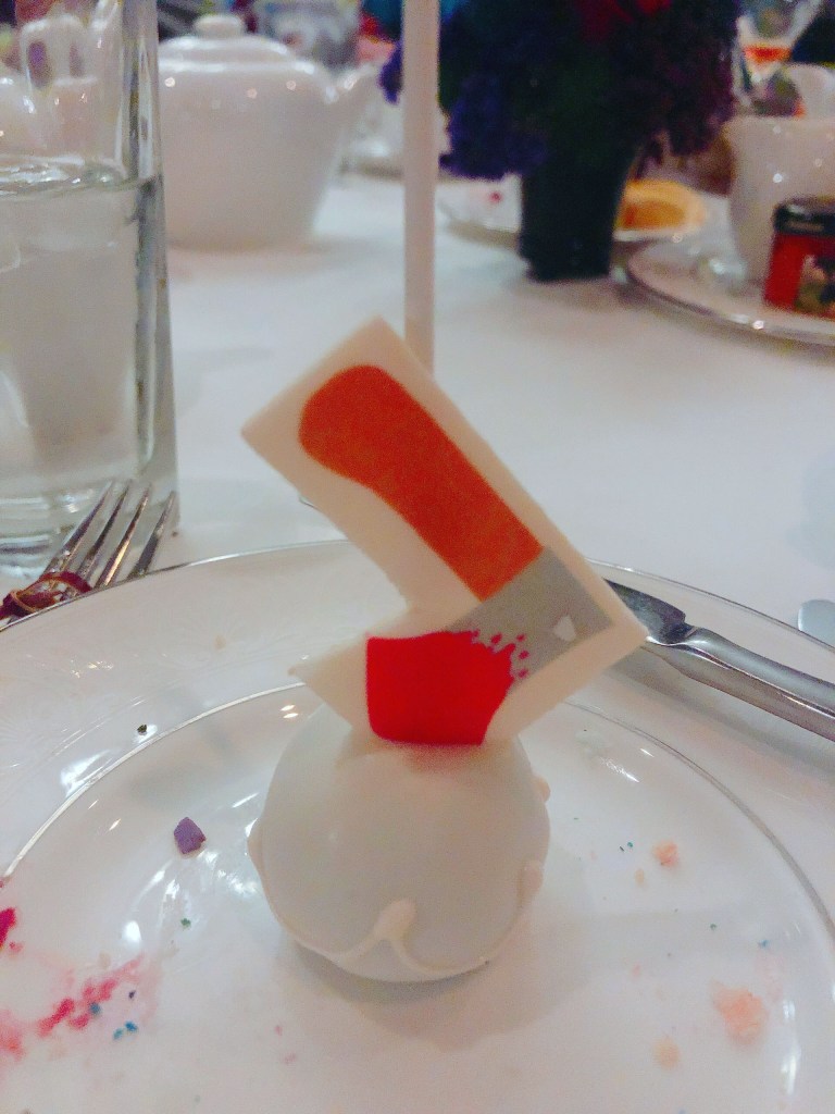 A white chocolate cake-pop with a edible miniature axe stuck inside of it.